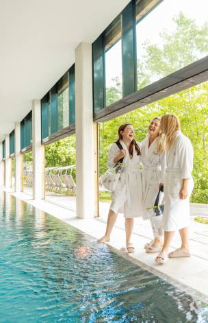 Freundinnen im Bademantel stehen am Pool