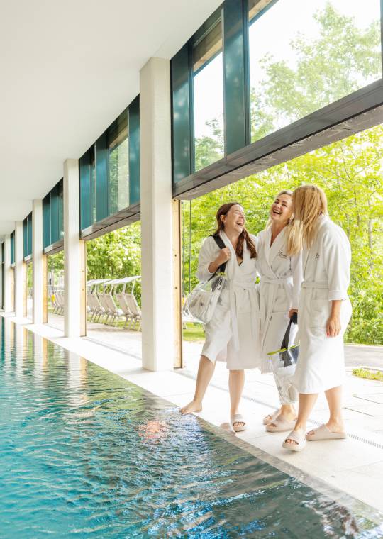 Freundinnen im Bademantel stehen am Pool