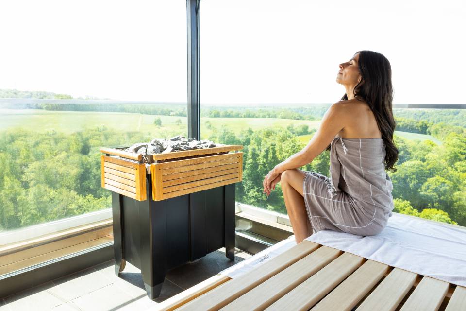 Frau sitzt in der Sauna mit Blick auf das Jagsttal