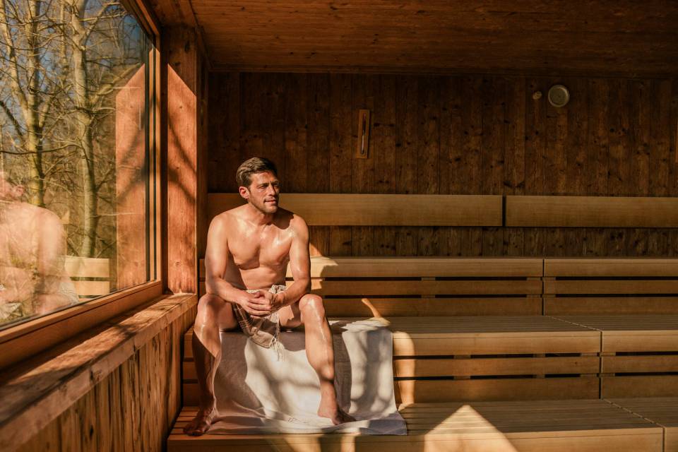 Mann sitzt in der Sauna mit Blick auf den Wald